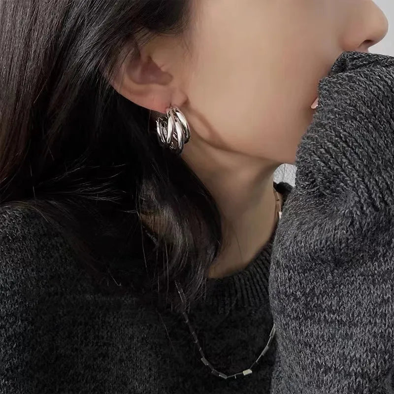 Profile of a person wearing lustrous silver geometric hoop earrings and a gray sweater | Oria Jewel