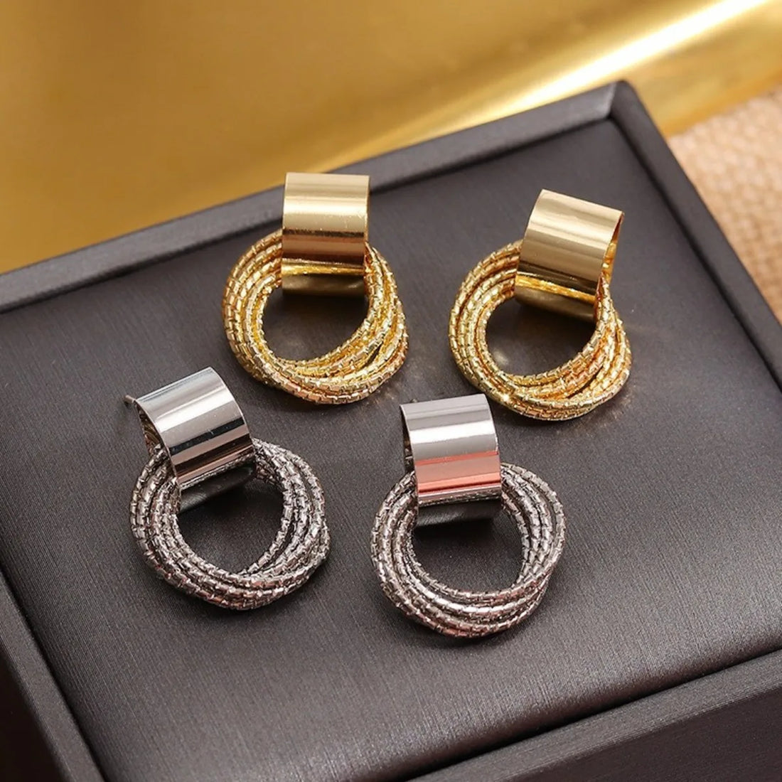 Four shiny gold and silver knot hoop earrings on a dark display tray | Oria Jewel