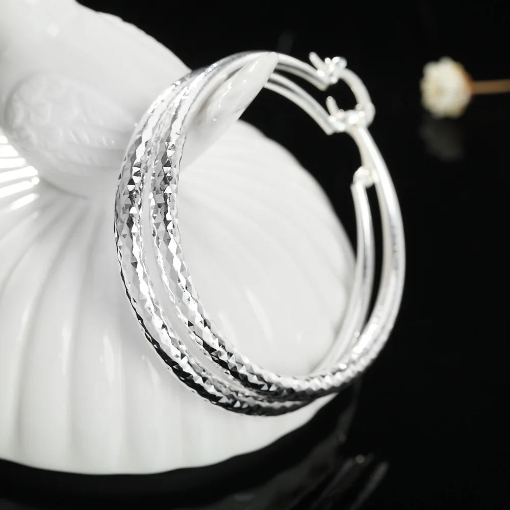 Gleaming textured and smooth Silver Hoop Earrings on a reflective black surface | Oria Jewel