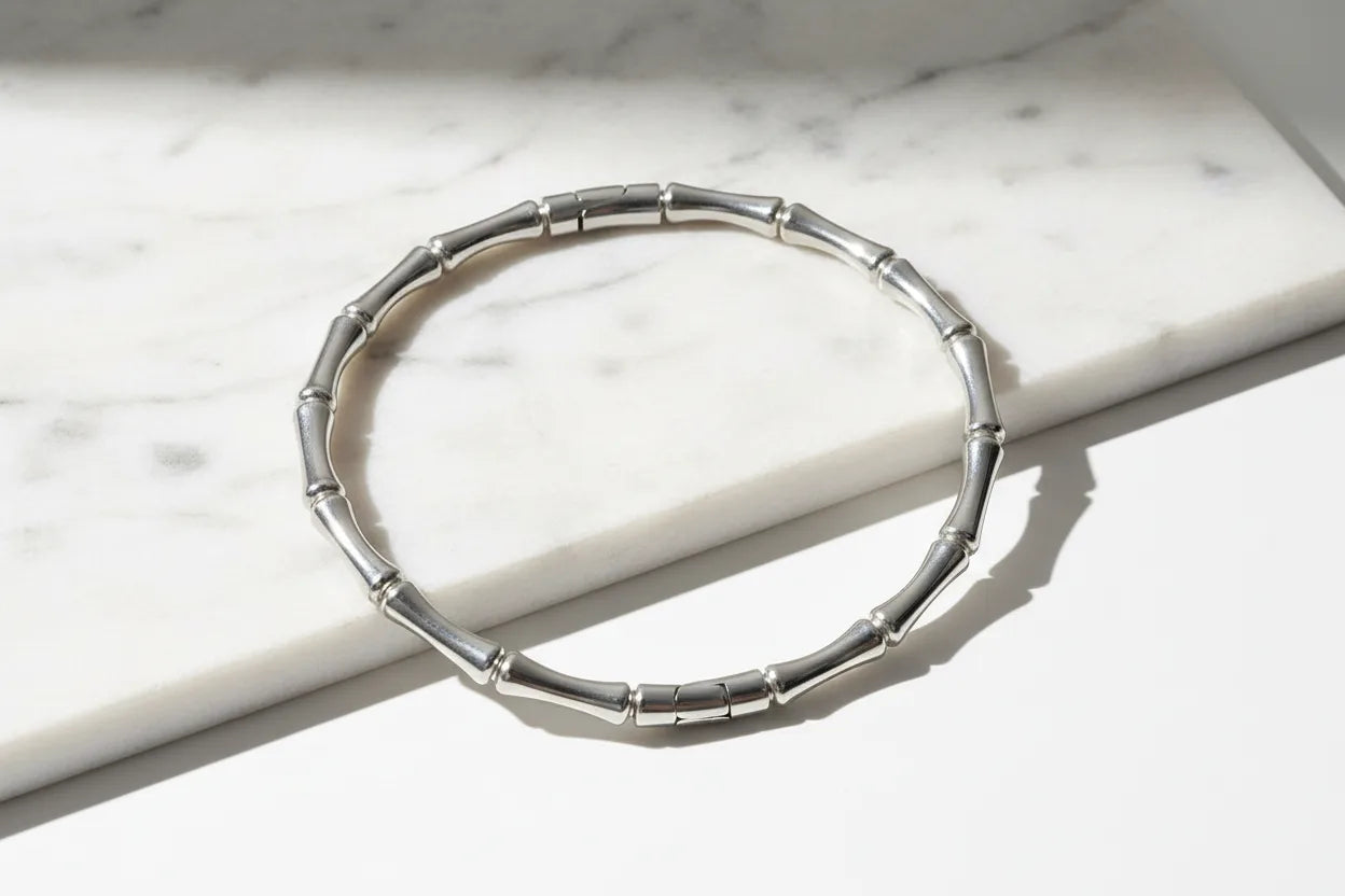 Close-up of a Silver Bamboo bangle Bracelet arranged on a white marble slab, bright directional light emphasizing the smooth metallic segments and modern bamboo-inspired texture | Oria Jewel