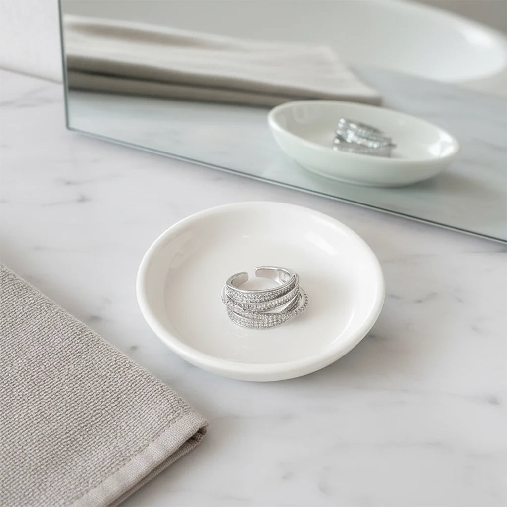 Silver CZ Wrap Ring placed in a white dish on a marble vanity with mirror reflection, emphasizing the layered wrap silhouette and shimmering CZ texture | OriaJewel