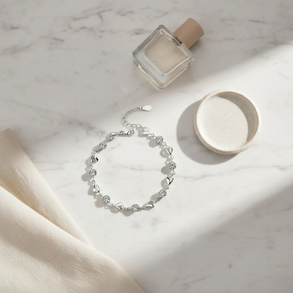 Minimal marble flat-lay of the Silver Heart Crystal Tennis Bracelet styled with a perfume bottle and ceramic dish, the bracelet catching natural sunlight and reflecting bright sparkles from each crystal and heart link | Oria Jewel