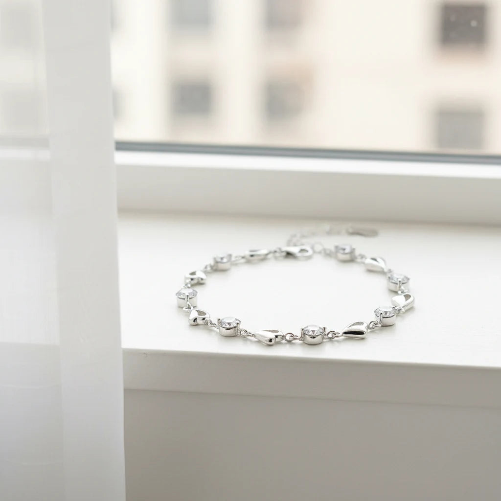 Bright window-sill shot of the Silver Heart Crystal Tennis Bracelet resting in a loose circle, its polished silver hearts and clear crystals contrasting beautifully with the clean white surface and blurred cityscape outside | Oria Jewel