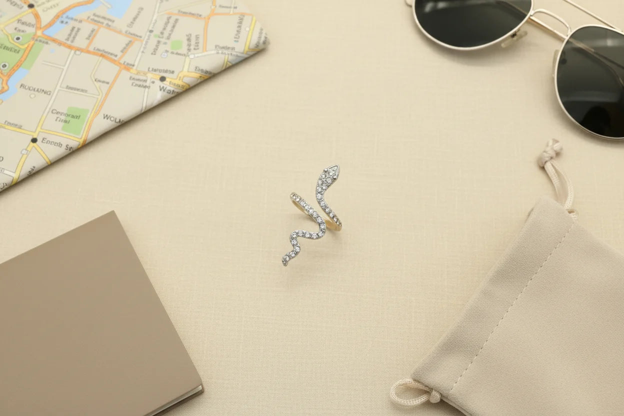 Silver Pavé Snake Wrap Ring flat-lay on a neutral linen surface with a map, sunglasses, notebook, and drawstring pouch, travel-inspired styling with the ring centered as the hero | OriaJewel
