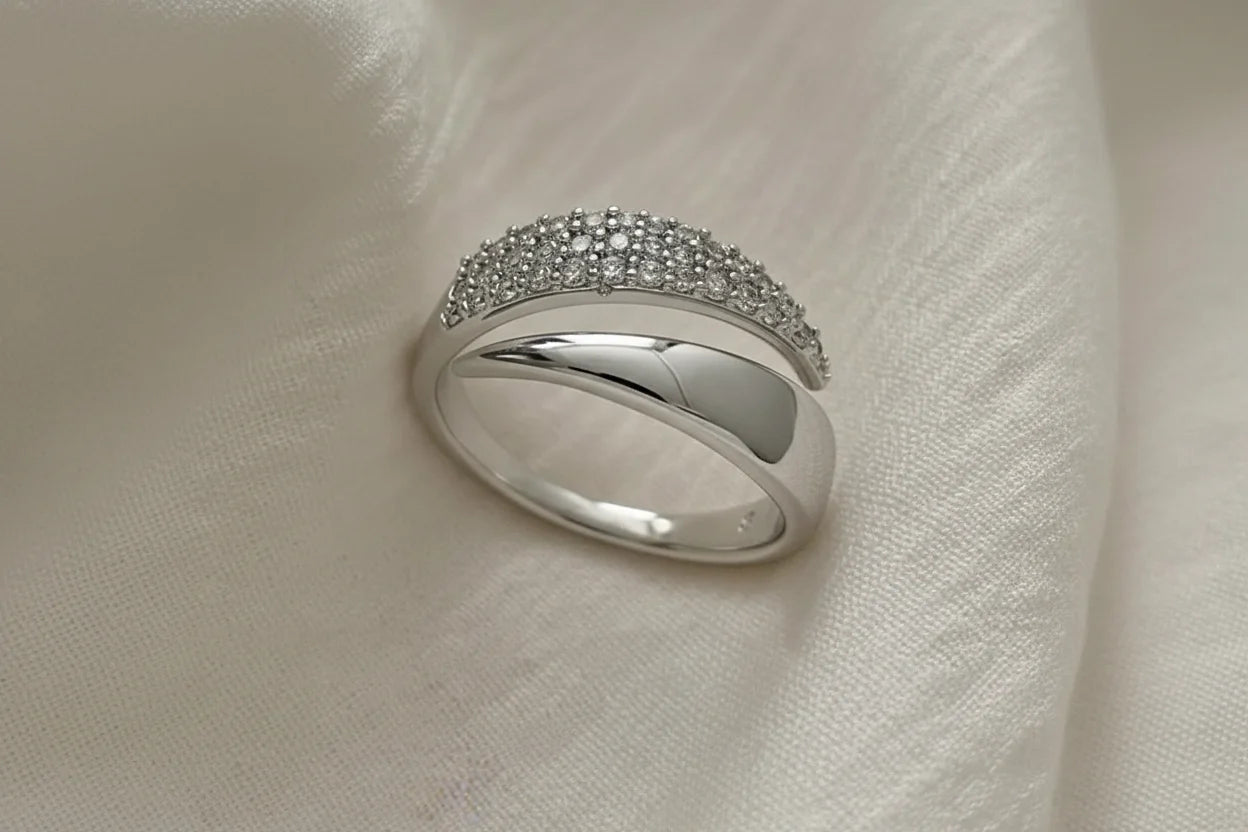 Macro close-up of a Silver bypass ring resting on ivory satin fabric, showing the pavé-studded arc and smooth overlapping bypass band in soft light | OriaJewel