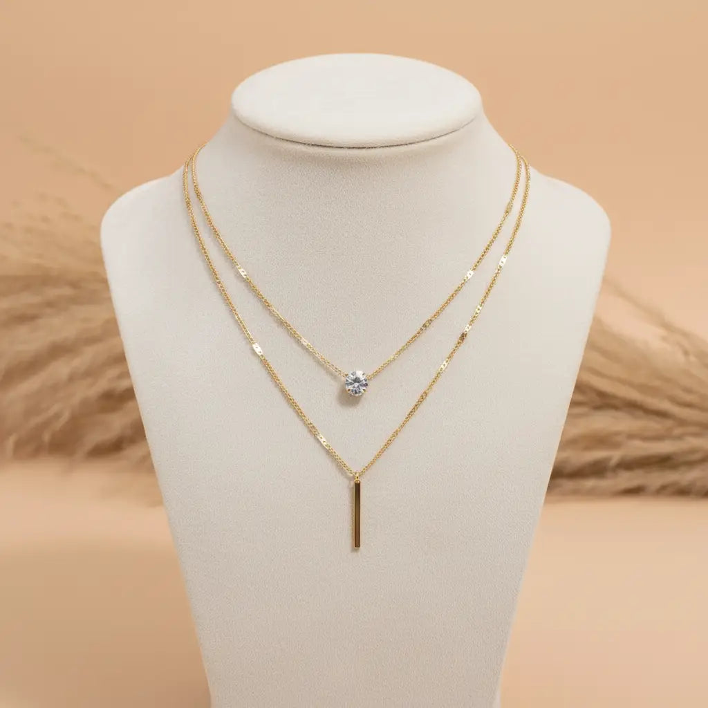 Gold Star Layered Necklace draped on a cream display bust against warm neutral backdrop, showcasing layered chains and crystal charm | Oria Jewel