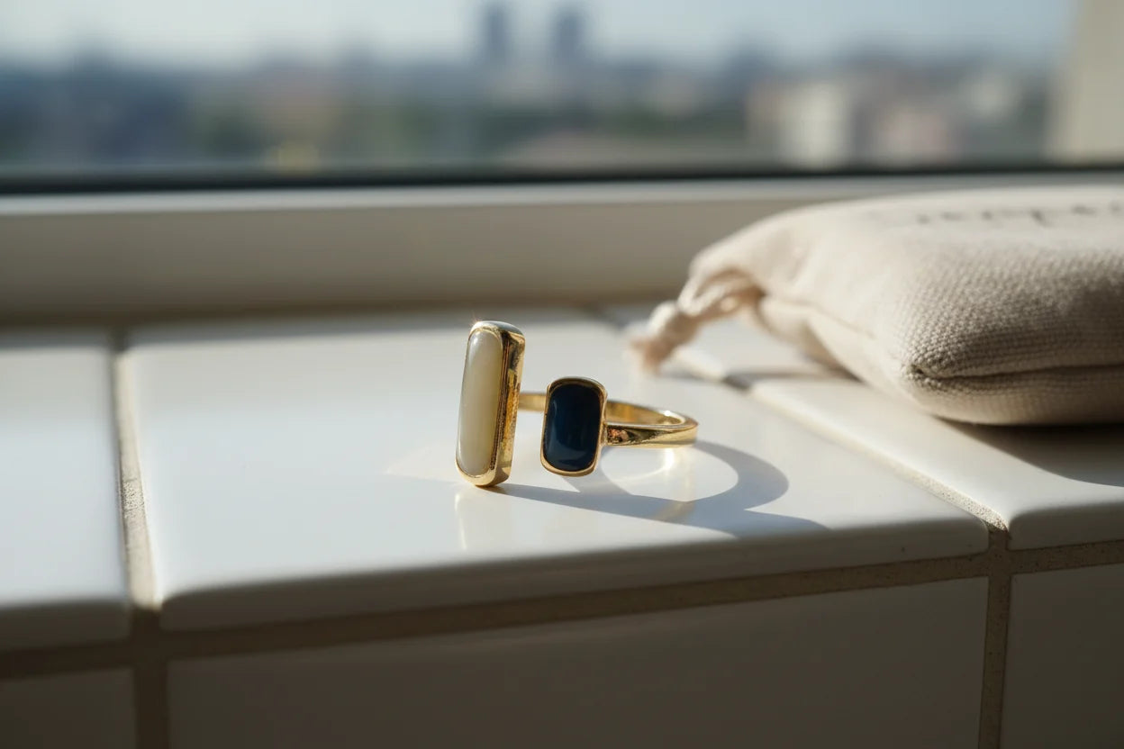 Two Stone Open Ring on a sunlit white tile windowsill, gold-tone open band with two rectangular stones (ivory and deep blue) beside a soft pouch | OriaJewel