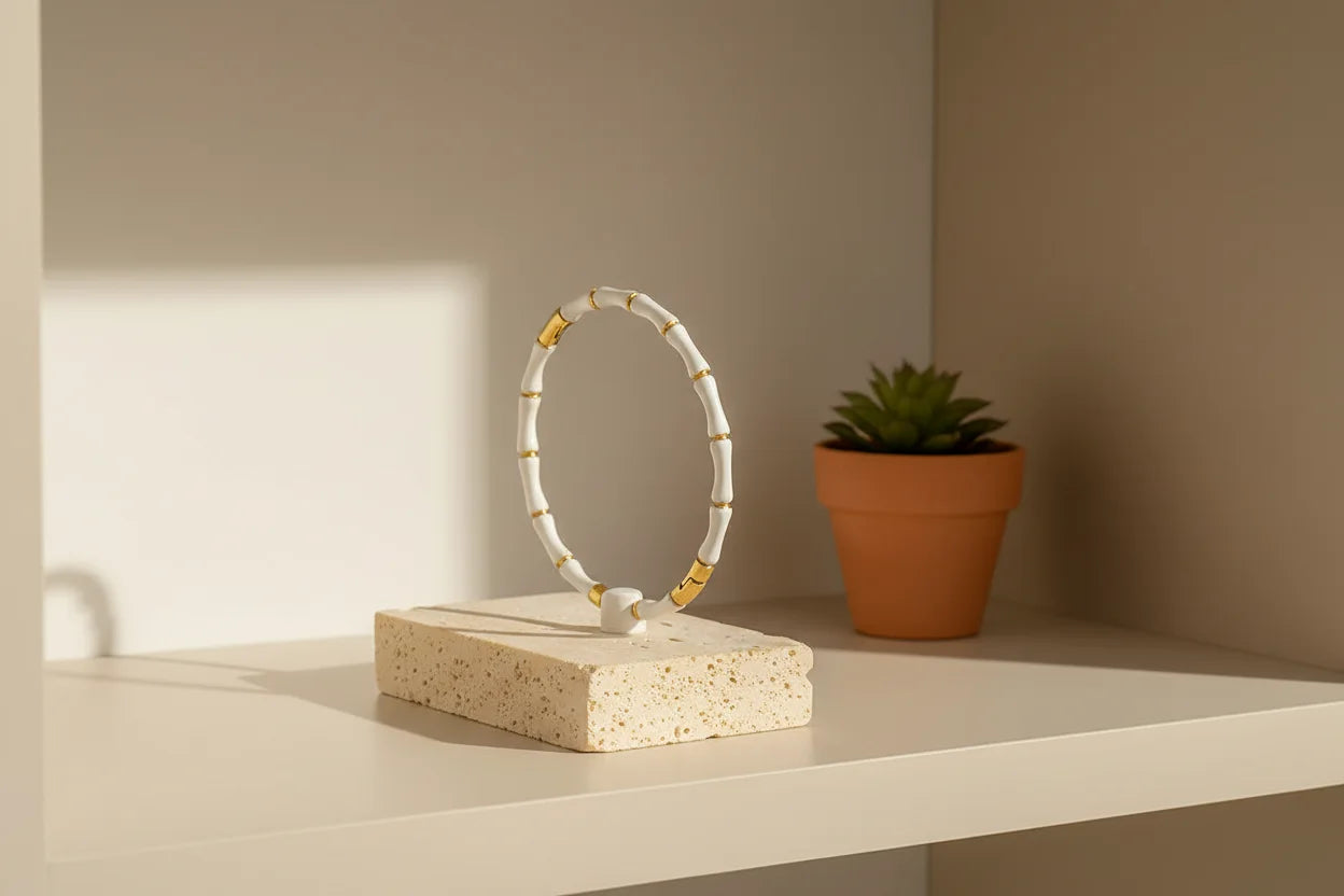 Minimal shelf display with a White Bamboo bangle Bracelet standing upright on a stone stand beside a small potted plant, styled in warm afternoon light | Oria Jewel
