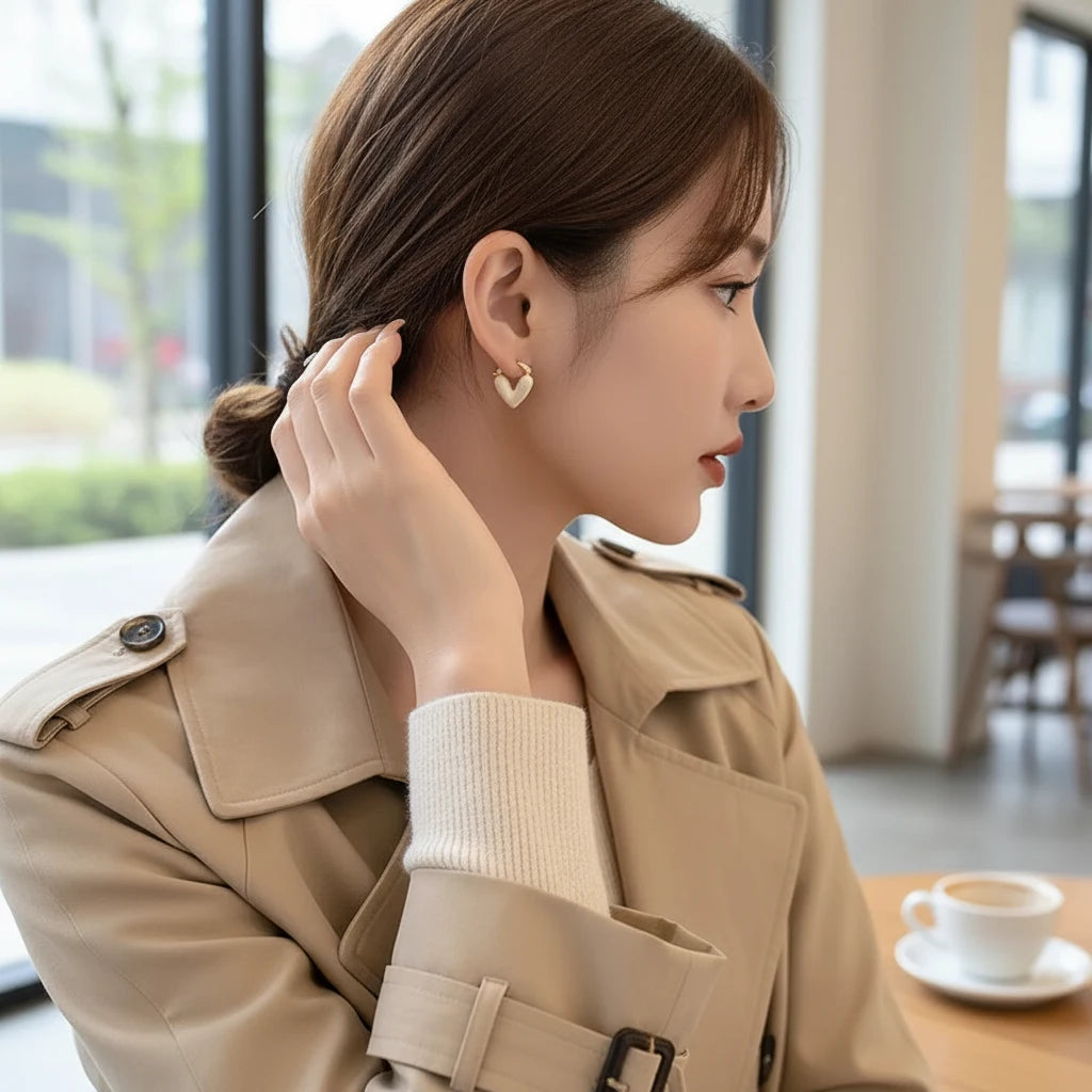 White Heart Huggie Hoop Earrings worn on model in cafรฉ setting | OriaJewel