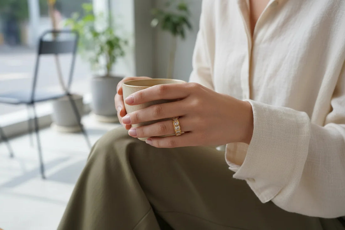 White stone band ring worn on a womanโs finger while holding a ceramic cup, lifestyle coffee-shop scene with soft daylight and a clean, minimal background | OriaJewel