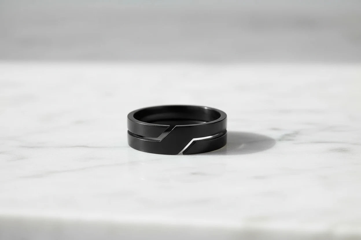 Wide Black Band Ring close-up on a light marble surface, focusing on the wide profile and clean geometric groove detail with soft highlights and a gentle shadow | OriaJewel