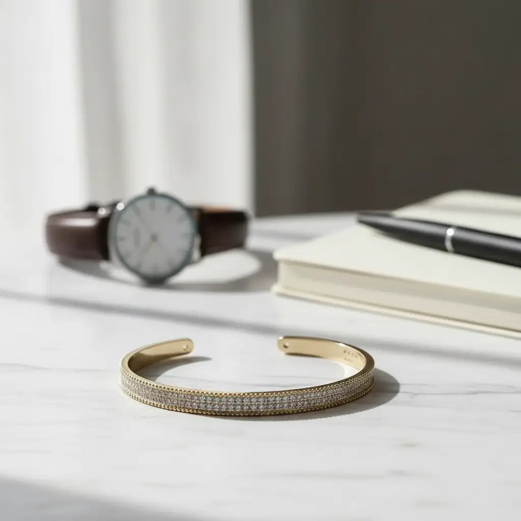 Minimal flat-lay of the gold Xaria Pavé Wrist Cuff resting on a white marble desk beside a classic watch, notebook, and pen, styled for a polished workday aesthetic | Oria Jewel