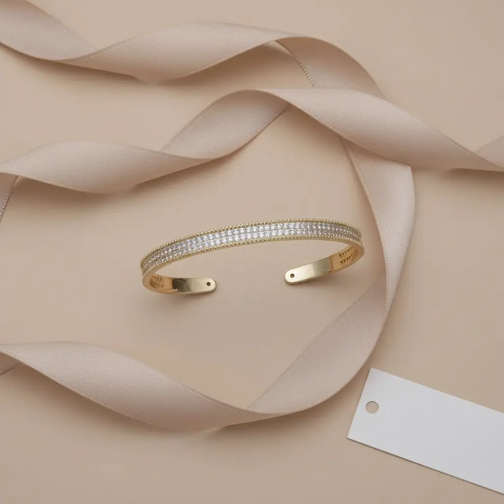 Gift-ready top view of the gold Xaria Pavé Wrist Cuff on a soft beige background, framed by a flowing satin ribbon and blank tag, perfect for presenting it as a special occasion gift | Oria Jewel