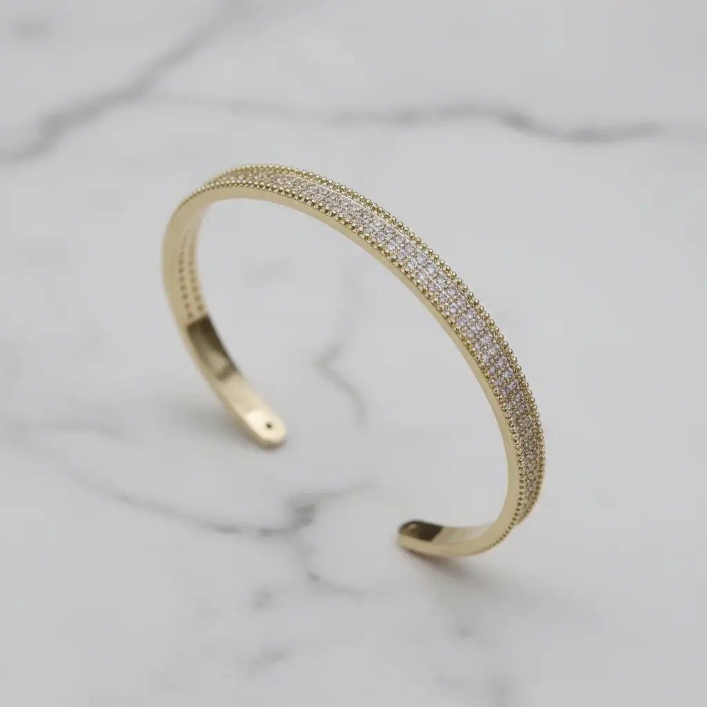 Side-by-side product display of the Xaria Pavé Wrist Cuff in gold and silver finishes on white marble, showing the slim open-cuff design and rows of sparkling pavé crystals | Oria Jewel