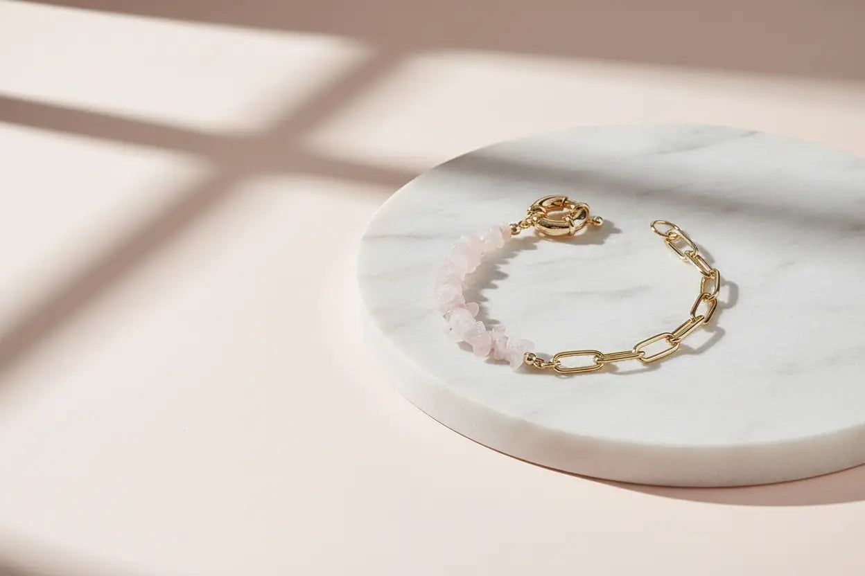 Gold chain bracelet with soft pink gemstone chips in an amethyst bead bracelet style placed on a round white marble slab over a blush backdrop, lit with gentle window shadows for a dreamy minimalist composition | Oria Jewel
