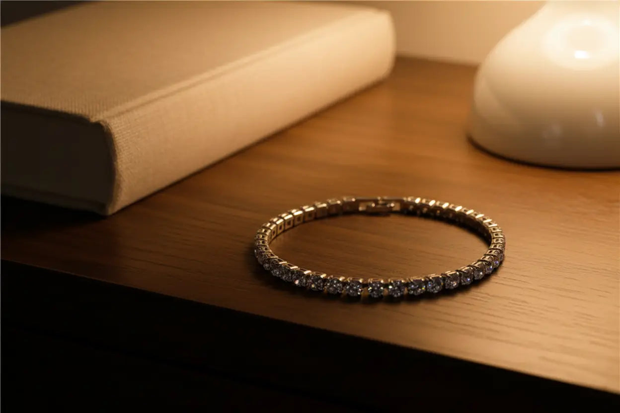 Close-up of a classic cz tennis bracelet laid in a perfect circle on a wooden bedside table beside a fabric-covered book and soft ceramic lamp, glowing in warm evening light | Oria Jewel