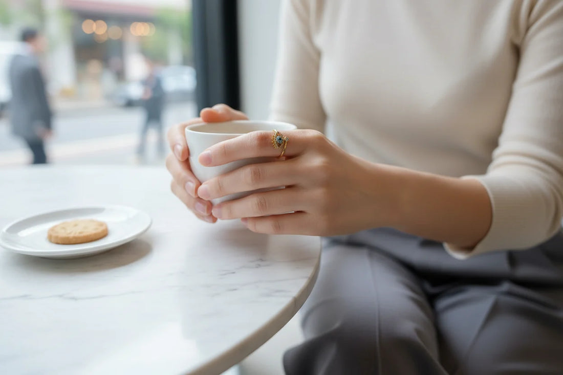 gold Evil Eye Ring worn while holding a cup at a cafΓ© table, natural daylight, subtle bokeh background, clear focus on the evil eye design | OriaJewel