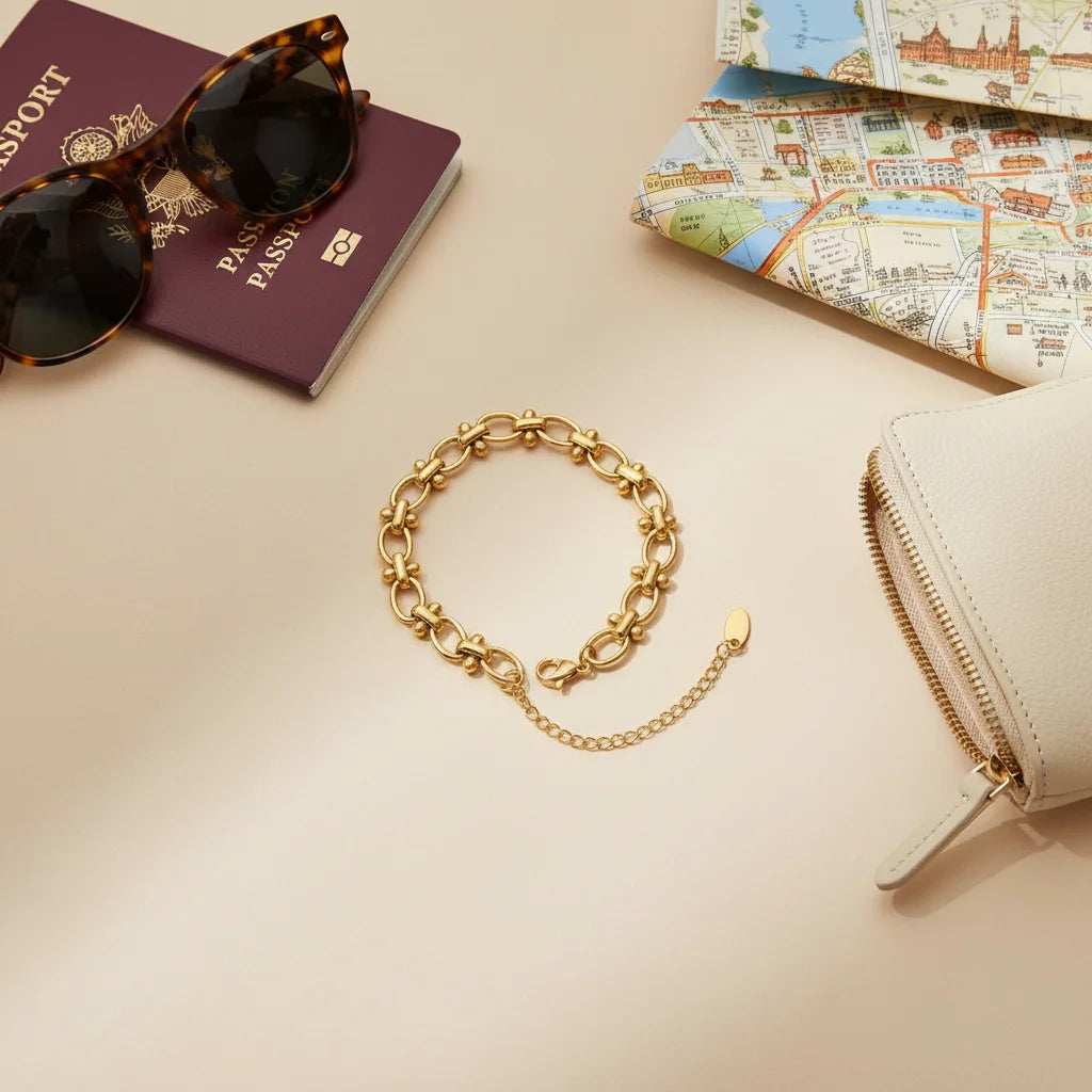 Travel-themed flat lay featuring a gold chain link bracelet beside a passport, city map, sunglasses, and a light wallet, styled as an elegant accessory for vacations and city breaks | Oria Jewel