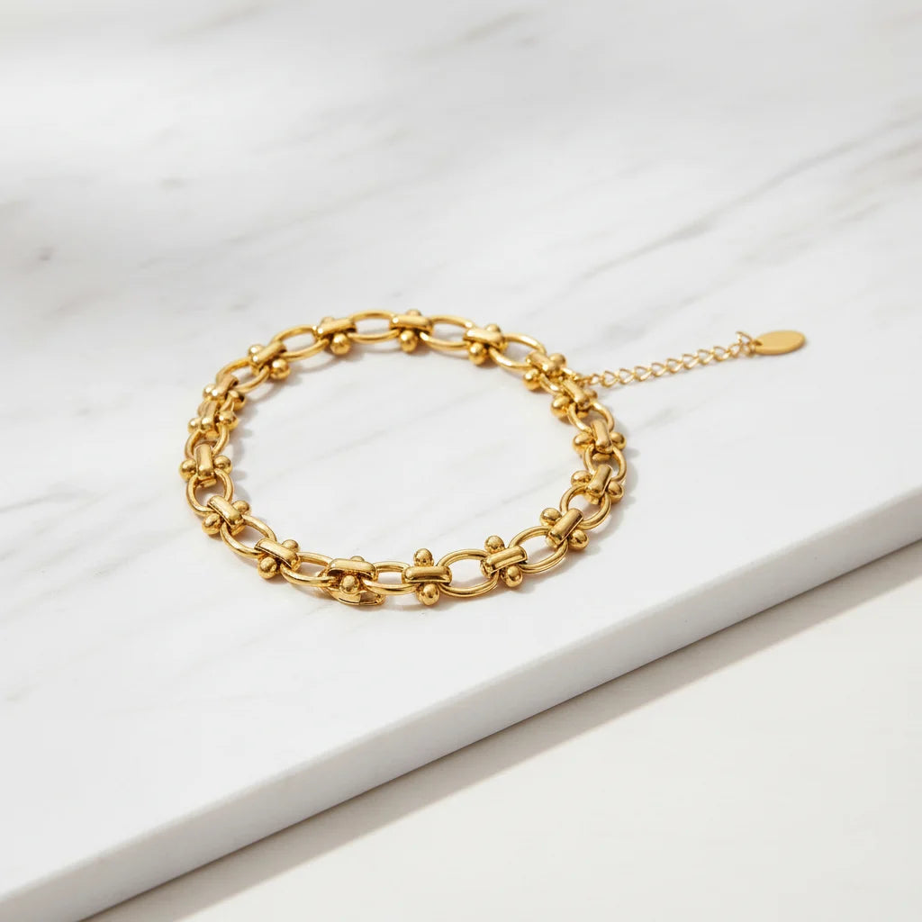 Detailed product image of a gold chain link bracelet arranged in a neat circle on a white marble surface, showing the textured links and delicate extender chain | Oria Jewel