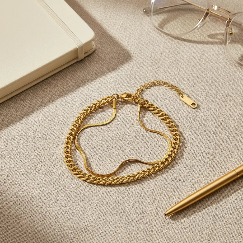 Gold double chain bracelet styled flat beside notebook, glasses and pen, suggesting chic desk-to-dinner accessorizing | Oria Jewel