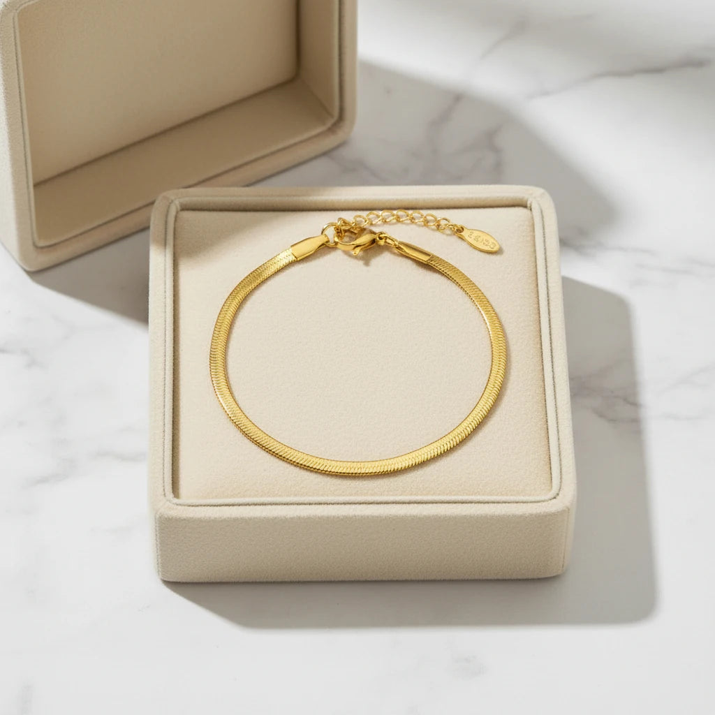 Gift-ready gold herringbone chain bracelet displayed inside an open beige jewelry box on white marble surface, lit by soft natural light | Oria Jewel