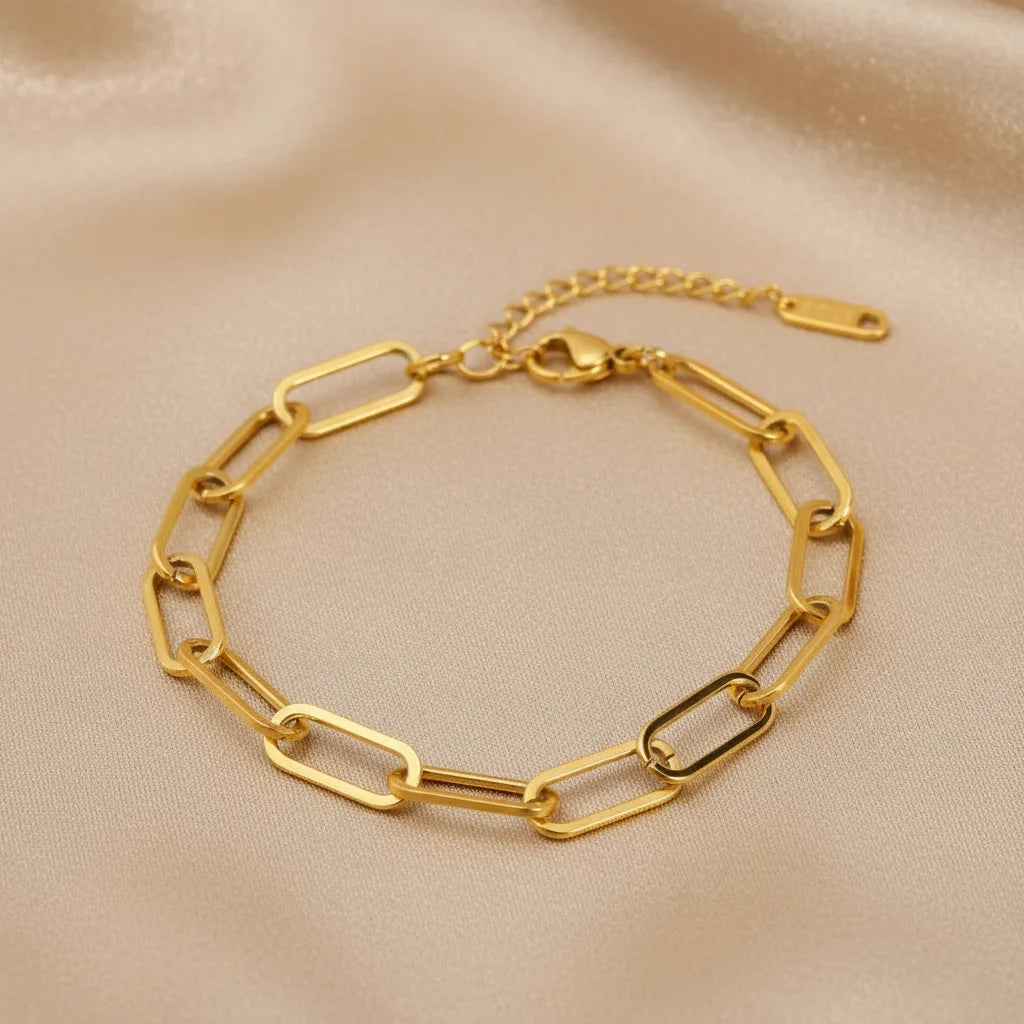 Gold paperclip chain bracelet laid flat on champagne satin fabric, highlighting its modern rectangular links and warm glow | Oria Jewel
