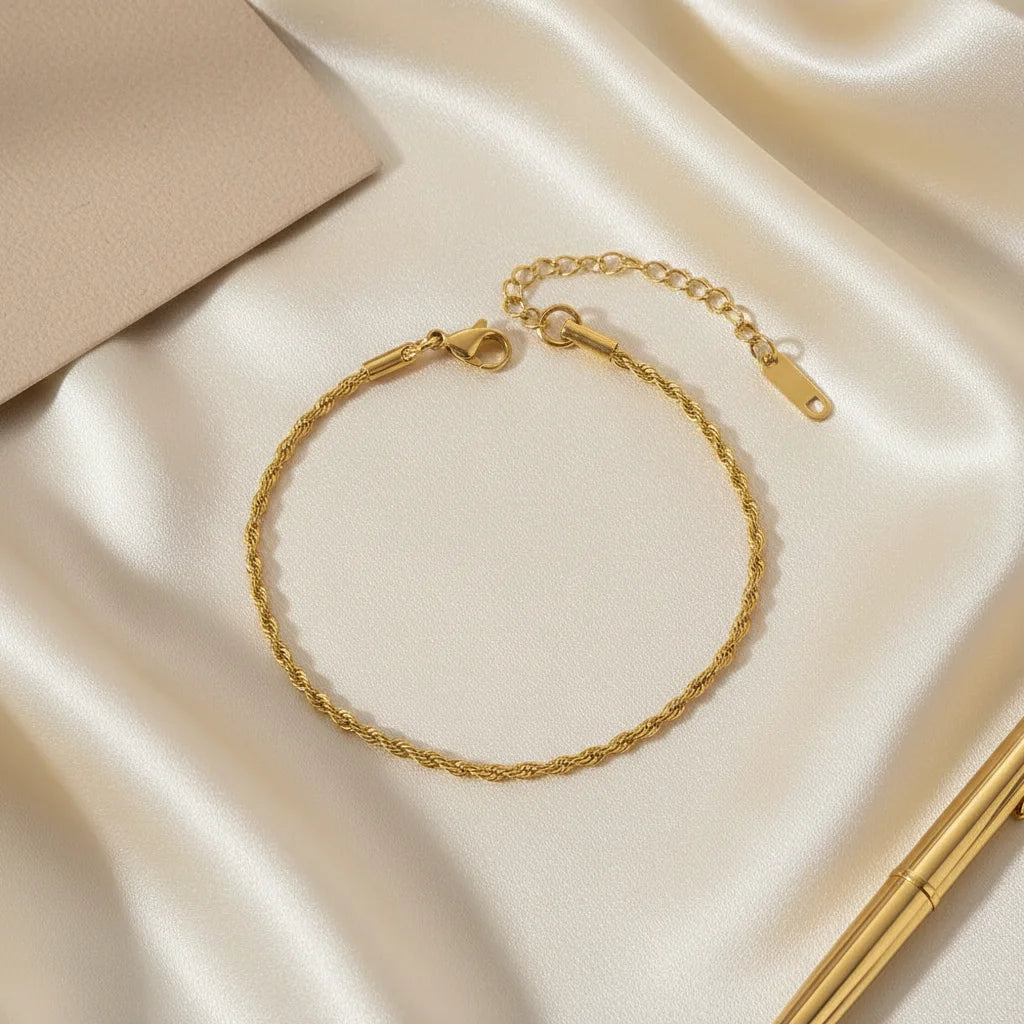 Elegant flat lay of a gold rope chain bracelet on champagne satin fabric beside a beige card and slim gold pen for a luxe feel | Oria Jewel