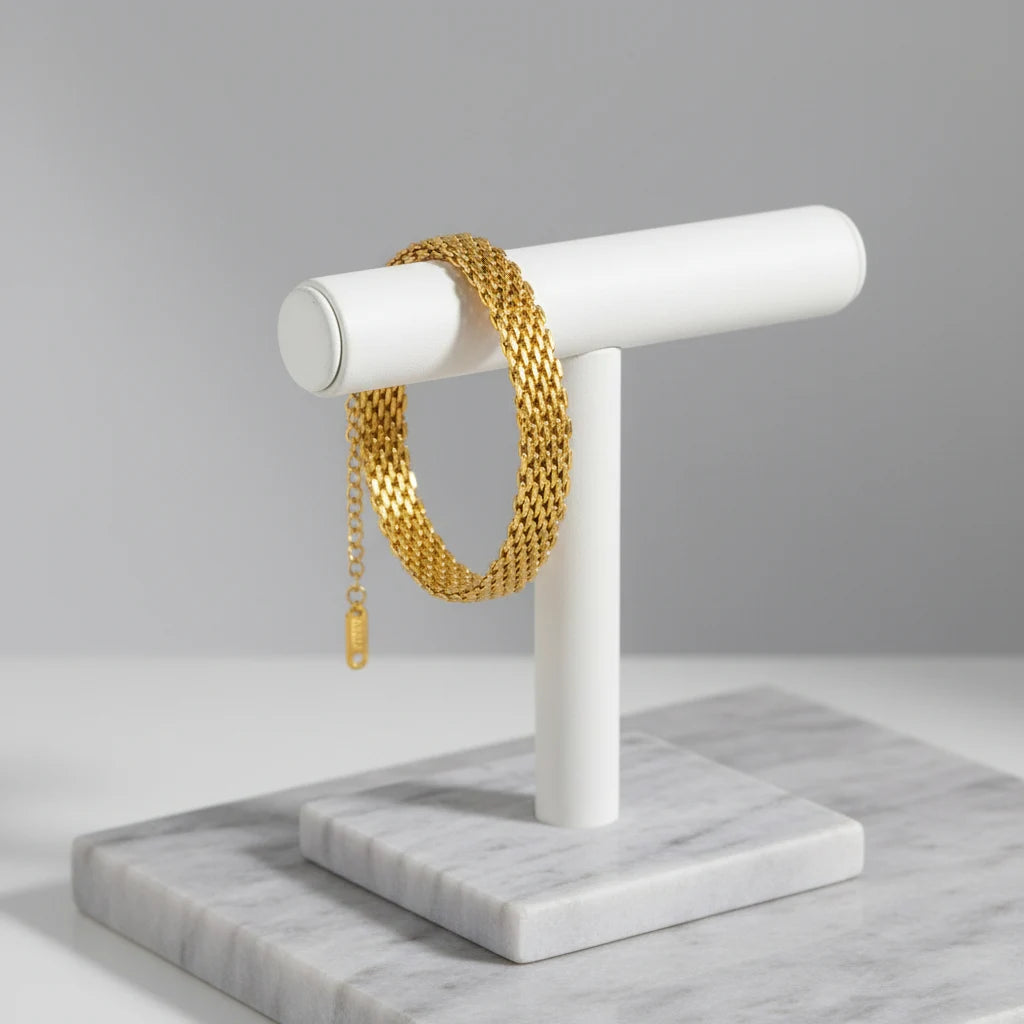 Gold wheat chain bracelet draped around a white jewelry stand on marble display surface | Oria Jewel