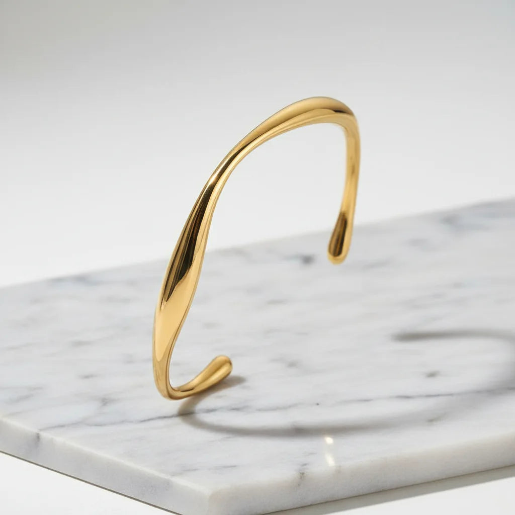 Minimalist gold cuff bracelet standing upright on a white marble slab, clean studio backdrop with soft shadows highlighting the smooth curved shape | Oria Jewel