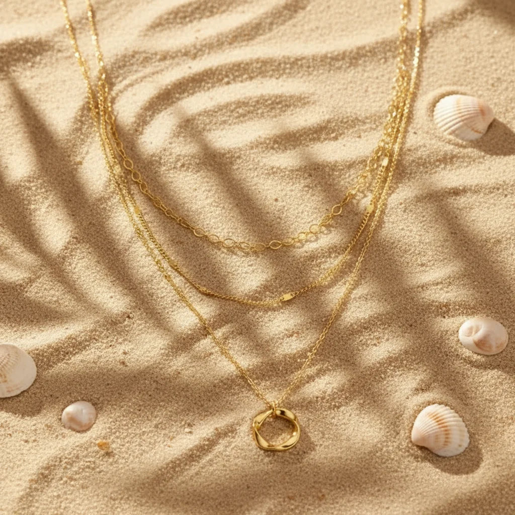 Multi Layered Gold Chain Necklace arranged on beach sand with seashells — soft sunlight highlighting golden texture | Oria Jewel