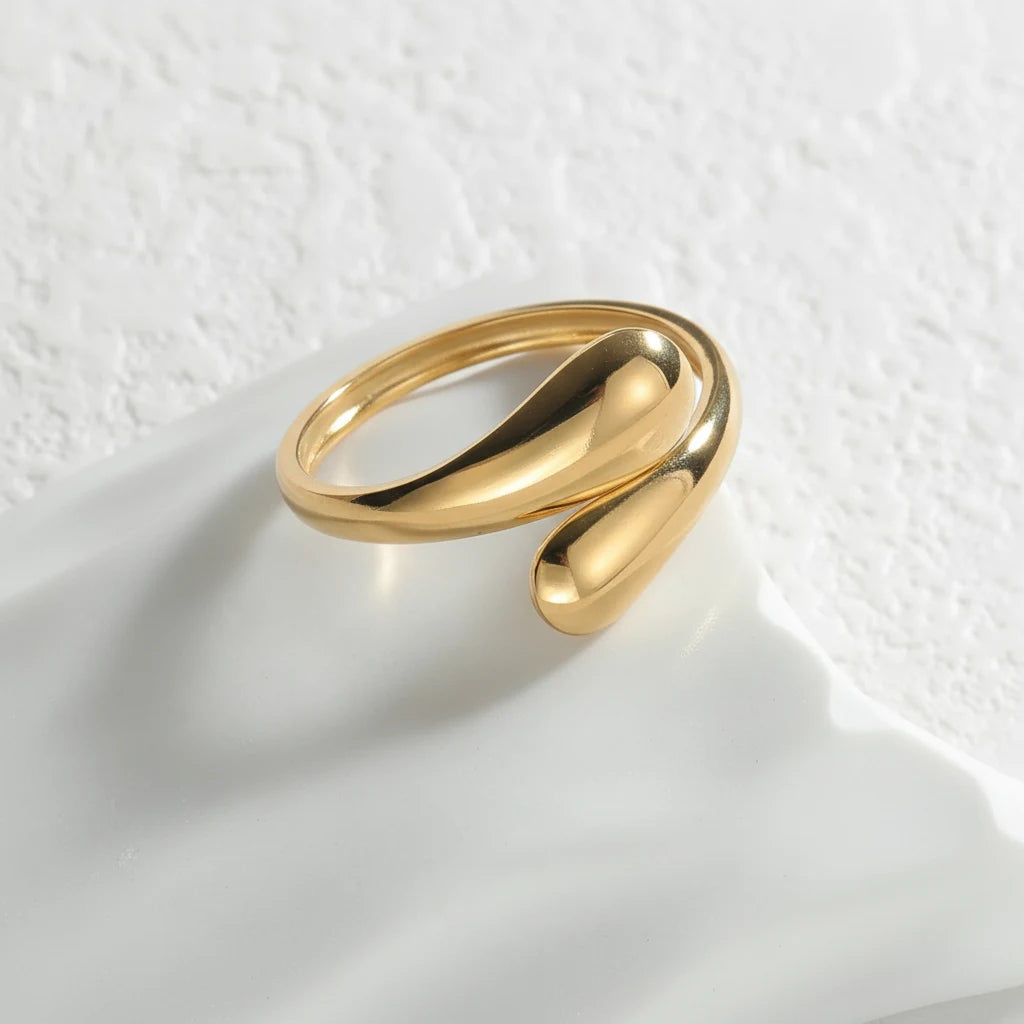 open gold wrap ring displayed on a white ceramic tray with a textured wall backdrop, polished wrap ends and gentle daylight emphasizing the adjustable open gap | OriaJewel