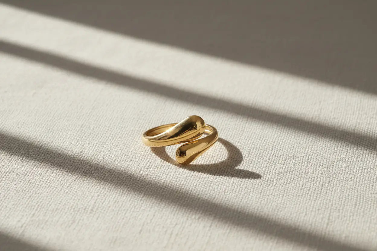 open gold wrap ring on textured beige linen under window-light stripes, showcasing the sleek crossover wrap silhouette and mirror-like shine | OriaJewel