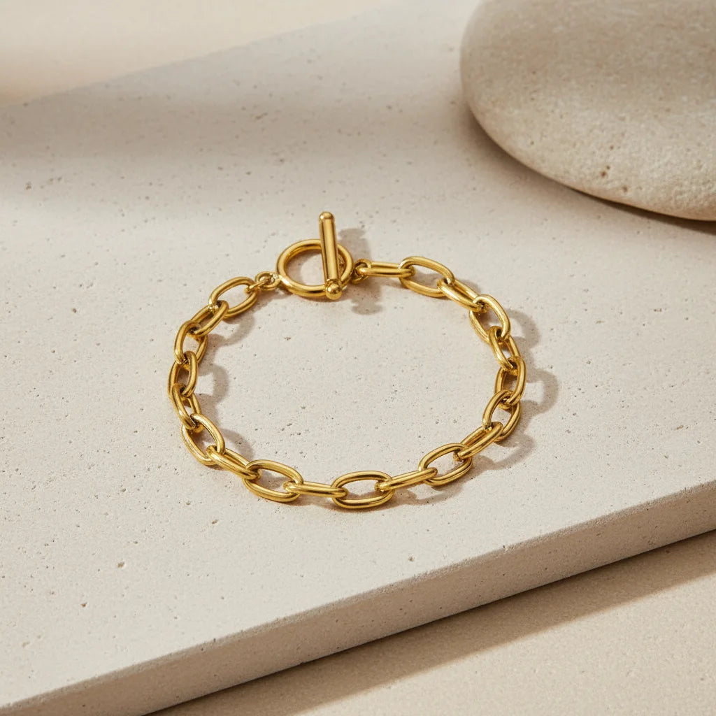 Minimal product shot of an oval link chain bracelet with toggle clasp displayed on textured beige stone blocks in warm natural light | Oria Jewel