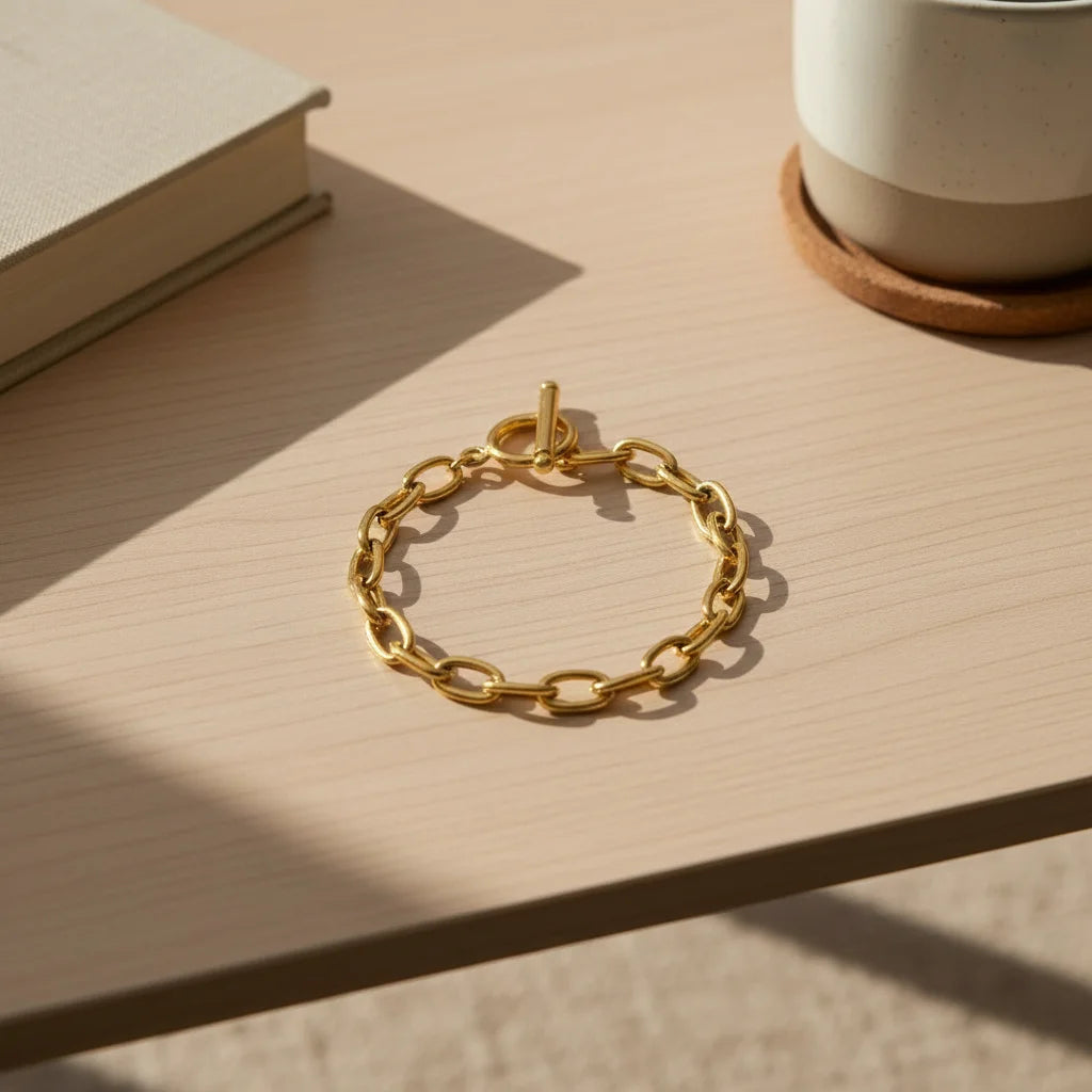 Oval link chain bracelet with toggle clasp styled on a light wooden desk beside a neutral book and coffee mug in afternoon sunlight | Oria Jewel