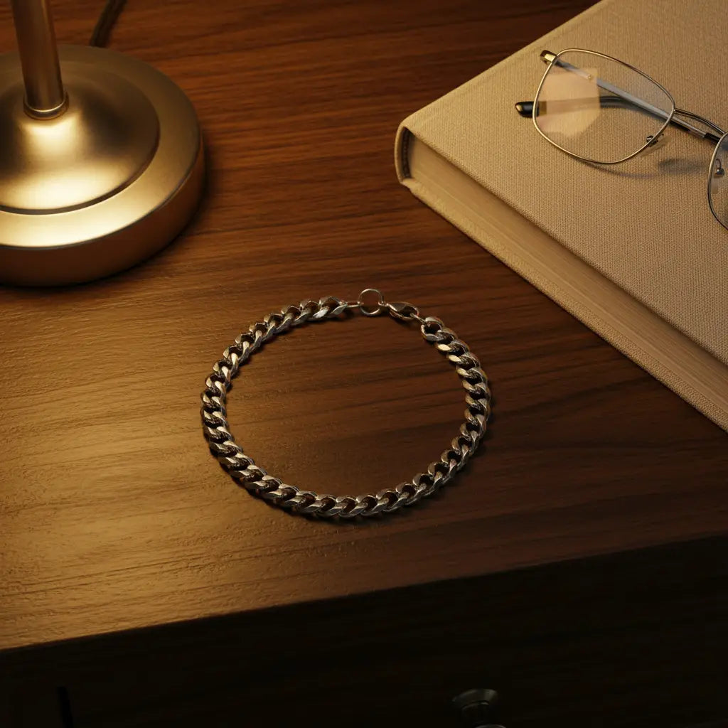 Cozy bedside flat lay with a glowing lamp and closed book on a wooden nightstand, featuring a classic silver chain bracelet arranged neatly in a circle beside them | Oria Jewel