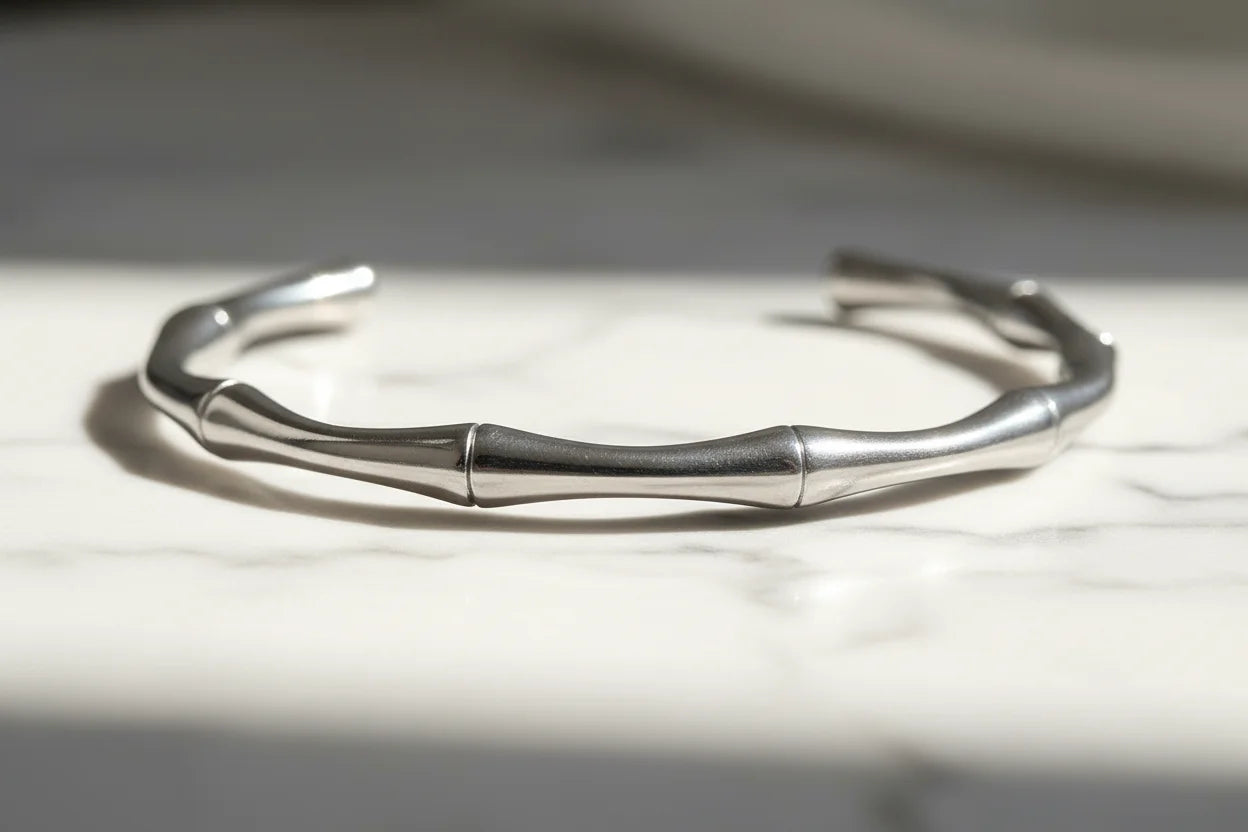 Close-up of a bamboo-textured silver cuff bracelet resting on a white marble surface, its smooth segmented design catching soft natural light | Oria Jewel