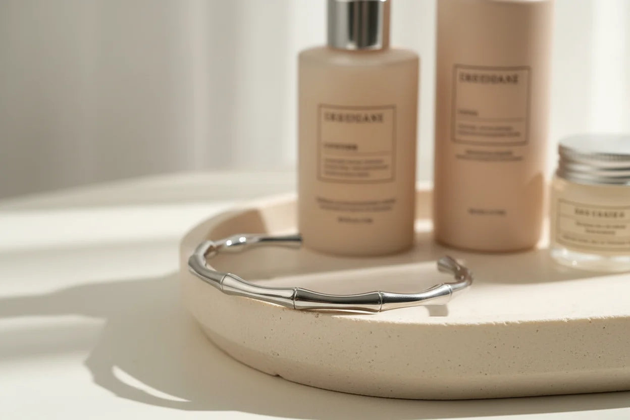 Self-care vignette with a polished silver cuff bracelet resting on a round ceramic tray beside neutral-toned skincare bottles in soft diffused daylight | Oria Jewel