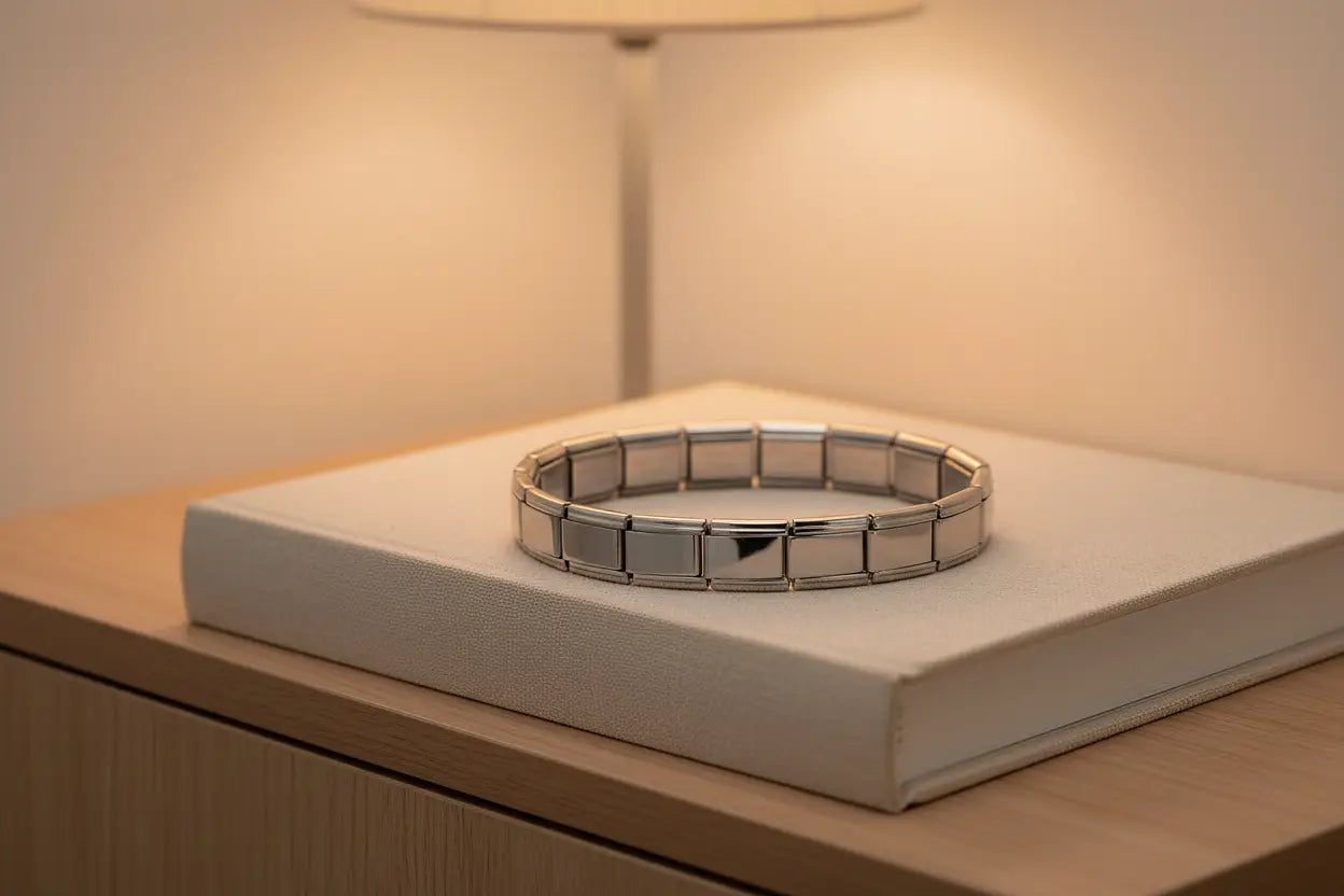 Cozy nightstand scene featuring a glowing lamp and a closed fabric-covered book, with a silver stainless steel stretch bracelets bracelets neatly resting on top, highlighting its clean, modern look for everyday wear | Oria Jewel
