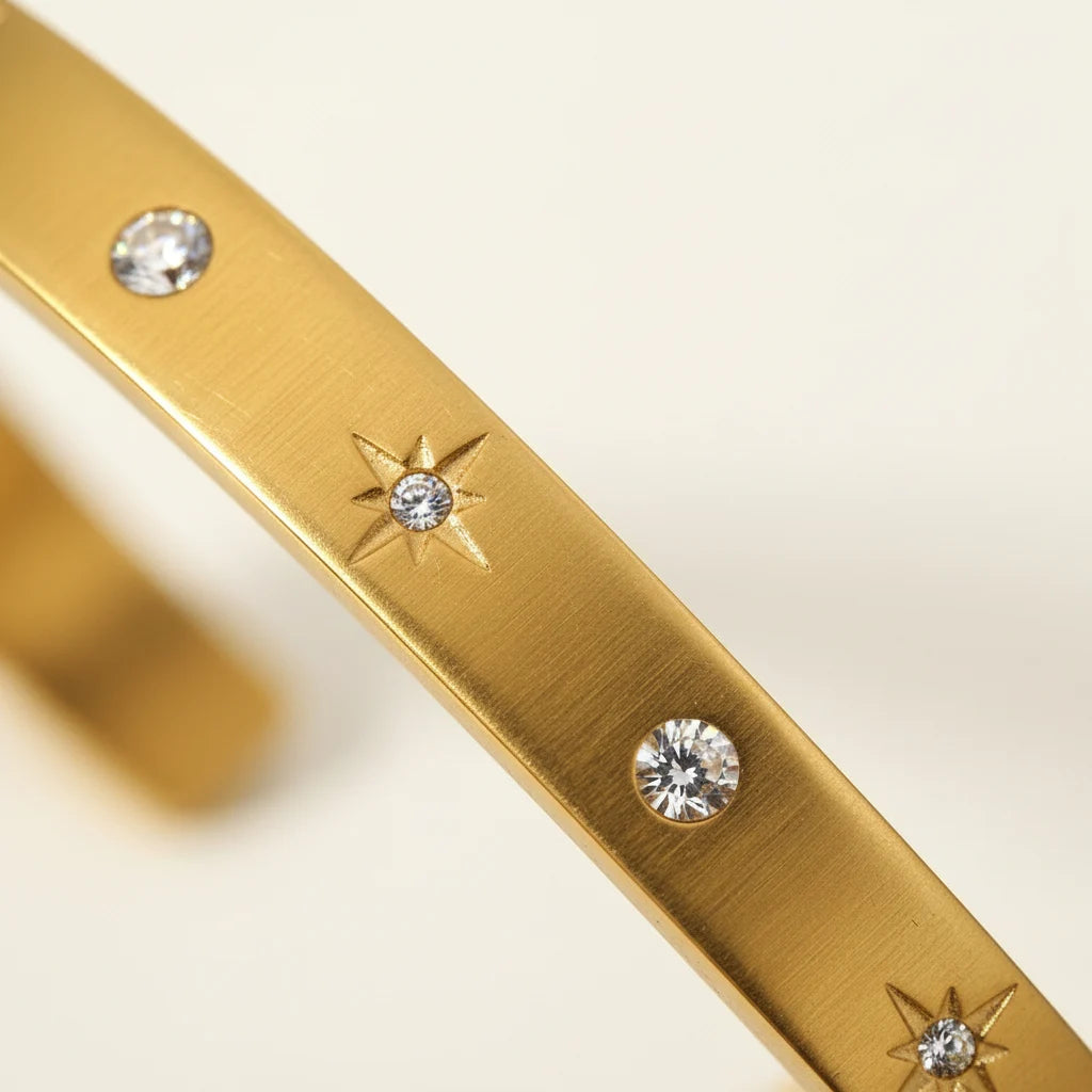 Close-up macro shot of a gold star cuff bracelet showing tiny engraved starbursts set with round crystals, highlighting the fine texture and luminous stones | Oria Jewel