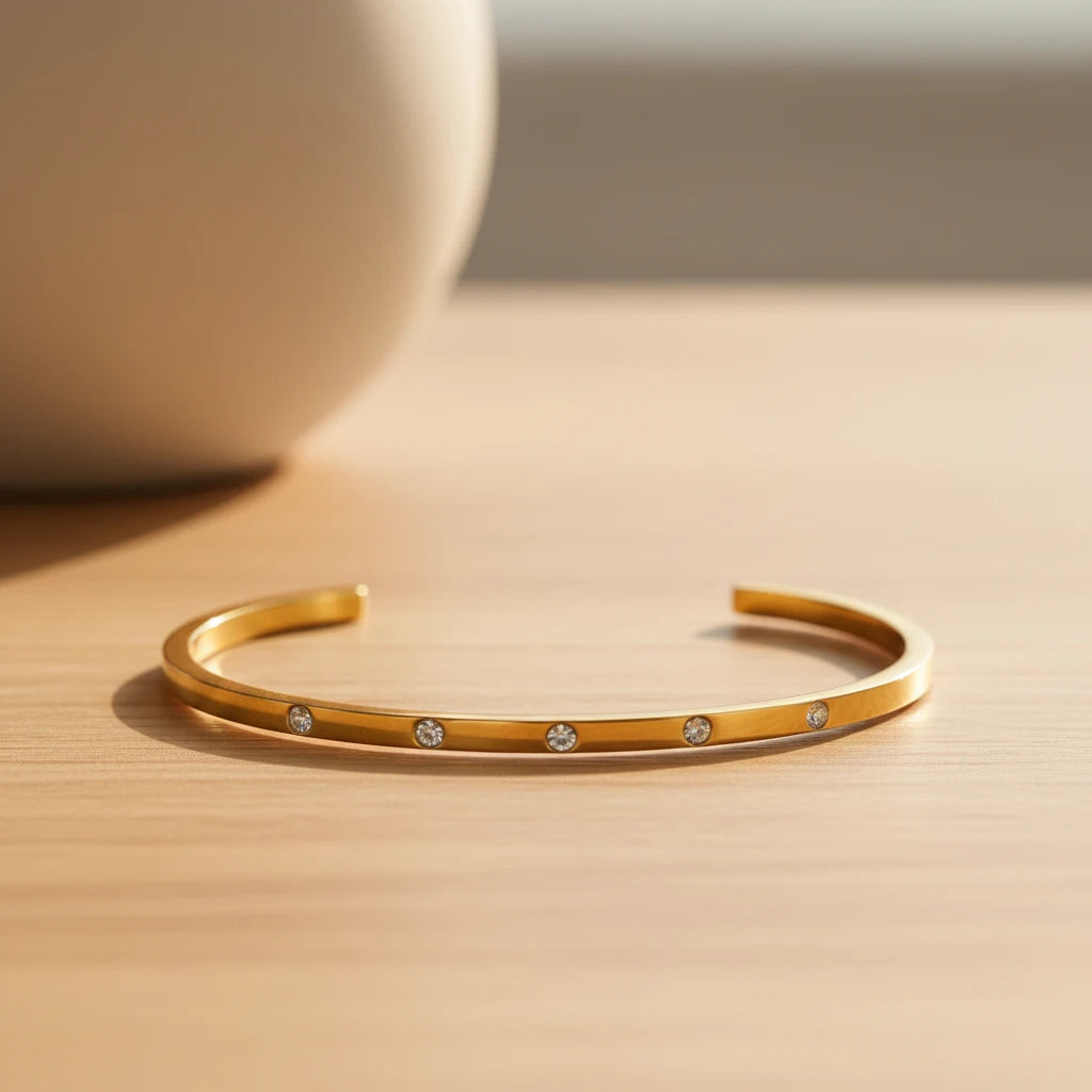 Minimalist scene with a thin gold cuff bracelet resting open on a light wooden surface in soft daylight, highlighting its slim profile and evenly spaced crystal accents | Oria Jewel