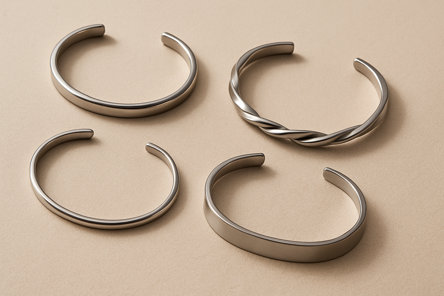 Wide flat lay of silver, gold, and black steel wrist cuffs on beige linen background, minimalist jewelry banner | Oria Jewe