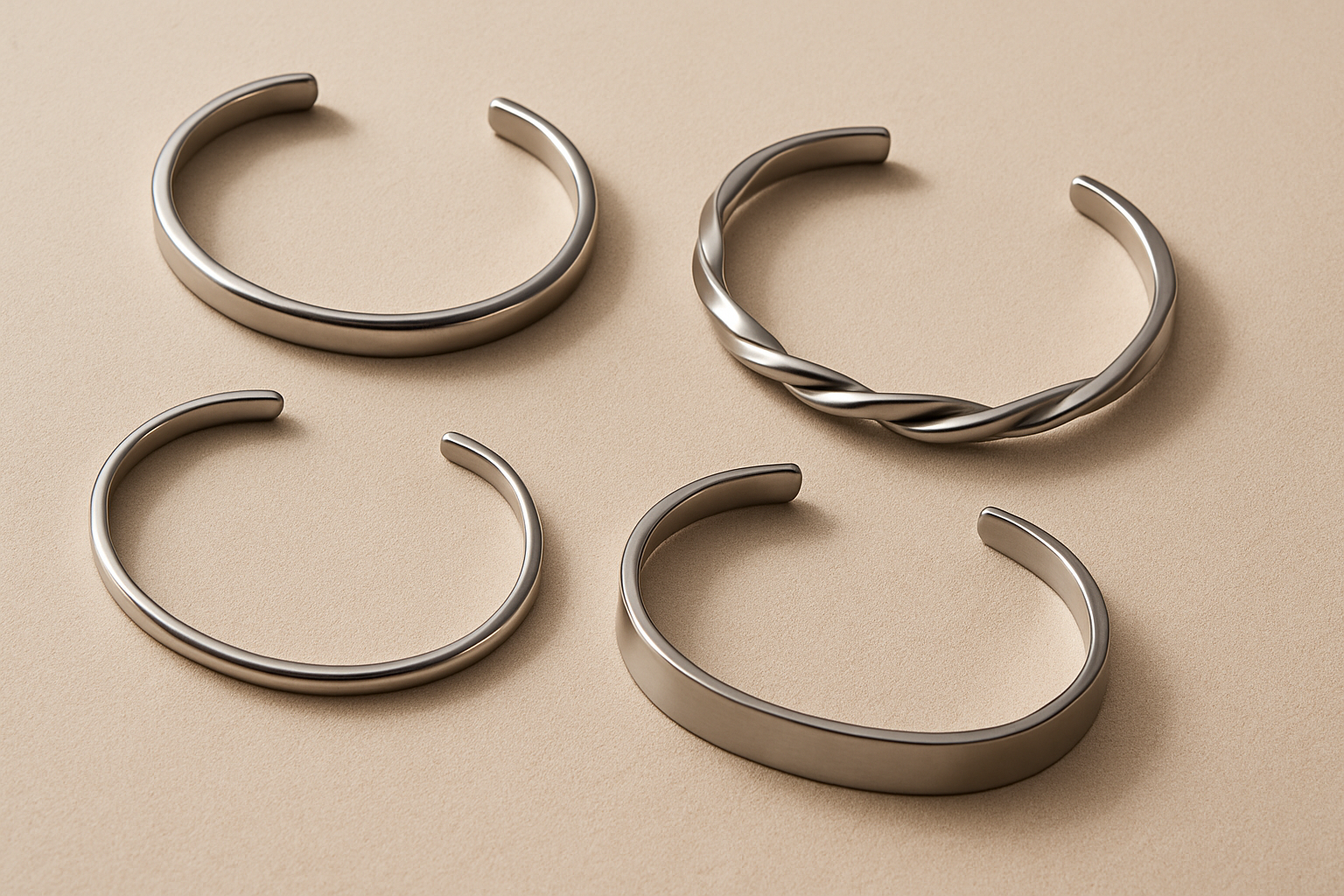 Wide flat lay of silver, gold, and black steel wrist cuffs on beige linen background, minimalist jewelry banner | Oria Jewe