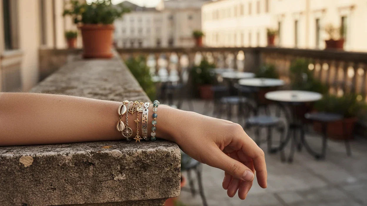 Woman’s wrist wearing layered gold and beaded Charm Bracelets Hero image on a sunny outdoor terrace | OriaJewel