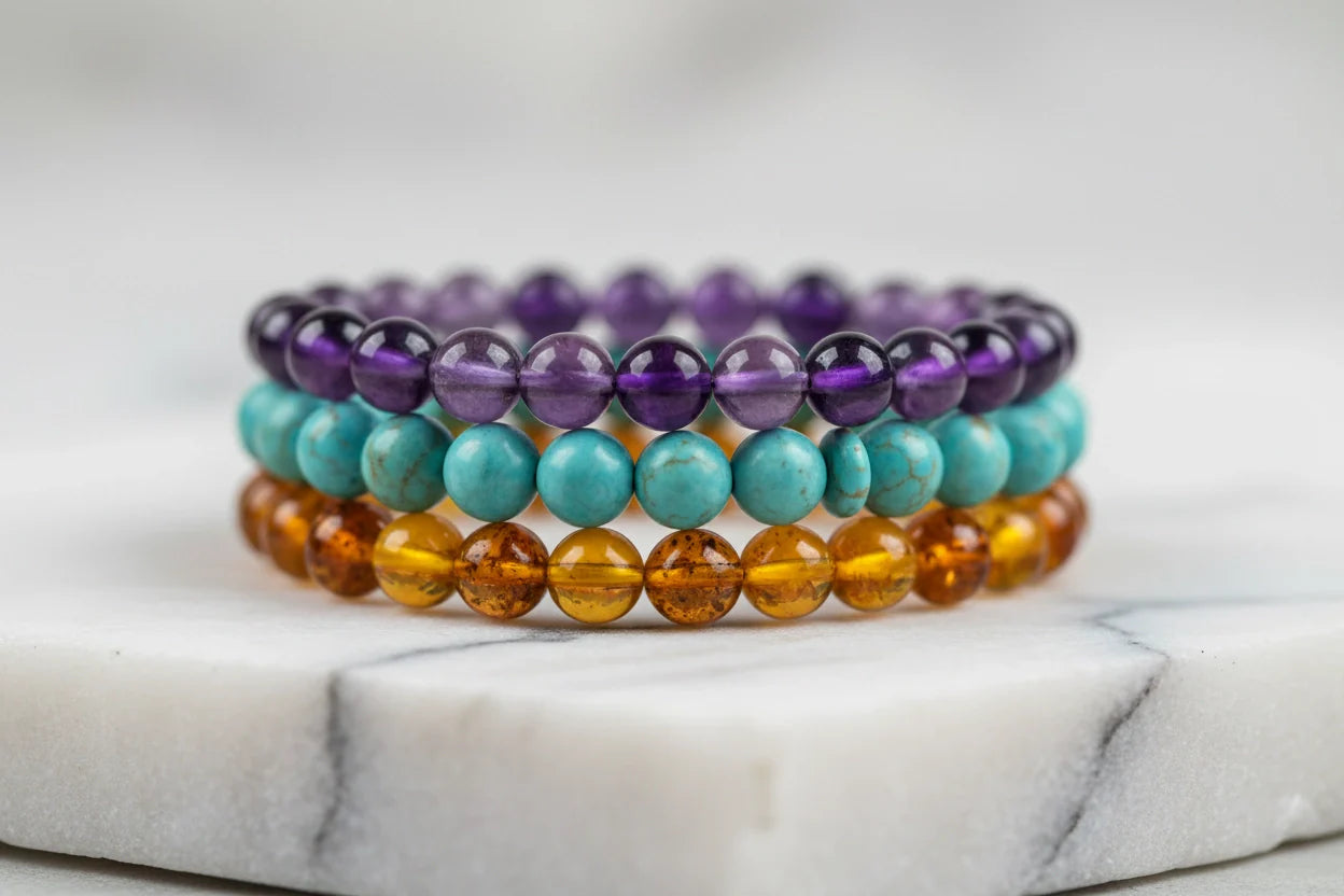 Stacked gemstone bead Stretch Bracelets in purple, turquoise, and amber tones on a white marble stand | OriaJewel