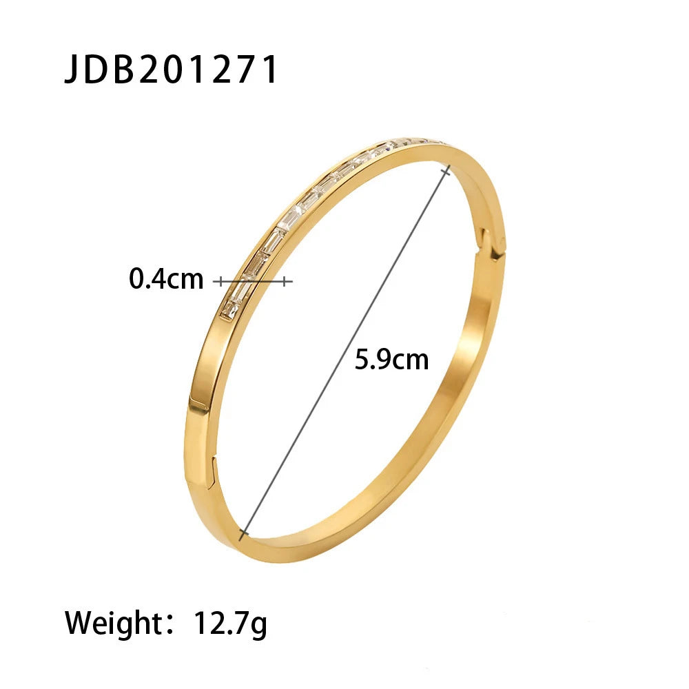 Product shot of a polished 14k gold hinged bangle bracelet on a white background, showing 5.9 cm inner diameter, 0.4 cm width, and a row of clear baguette-style stones on the top | Oria Jewel