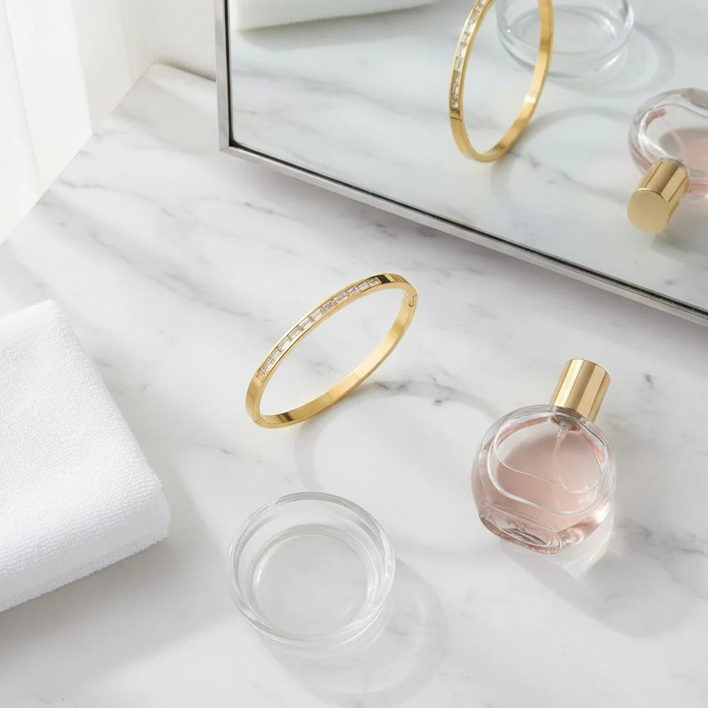 Flat lay on a marble vanity with mirror, perfume bottle, towel, and a sleek 14k gold hinged bangle bracelet placed in the center, highlighting its slim profile and stone detailing | Oria Jewel