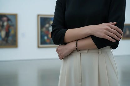 Woman in a modern art gallery wearing a Black Bamboo bangle Bracelet with gold accents, styled with black top and cream trousers, minimalist chic look | Oria Jewel