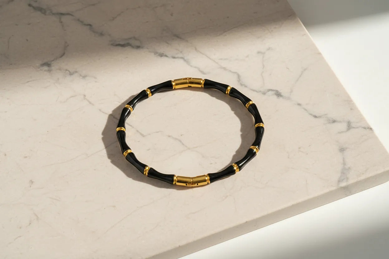 Close-up of Black Bamboo bangle Bracelet with polished gold links displayed in a circle on a light marble slab with soft shadows | Oria Jewel