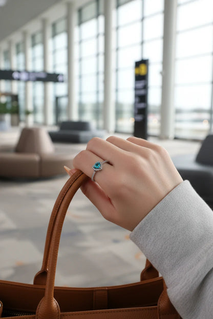 Blue Heart Halo CZ Ring worn on a hand holding a brown leather bag handle in a bright modern terminal setting, highlighting the blue heart halo sparkle on the finger | OriaJewel