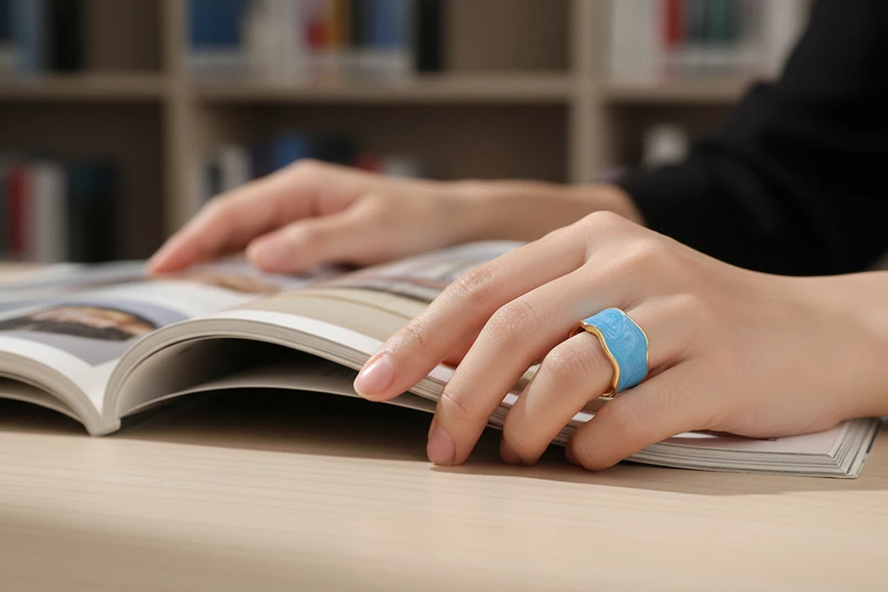 Hand wearing Blue Marble Open Wave Ring while reading an open book, soft library background | OriaJewel
